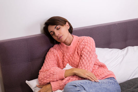 Une femme se repose sur son lit, un coussin posé sur son ventre, se demandant : est-ce que le miel constipe ?