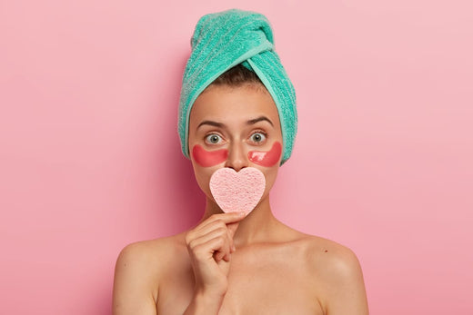 Une jeune femme avec une serviette sur la tête, tient une éponge en forme de cœur, illustrant la réalisation d'un masque pour les lèvres.