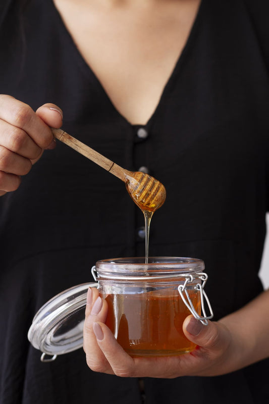 Miel pour la peau : une femme tenant un pot dans ses mains et une cuillère trempée dans le miel