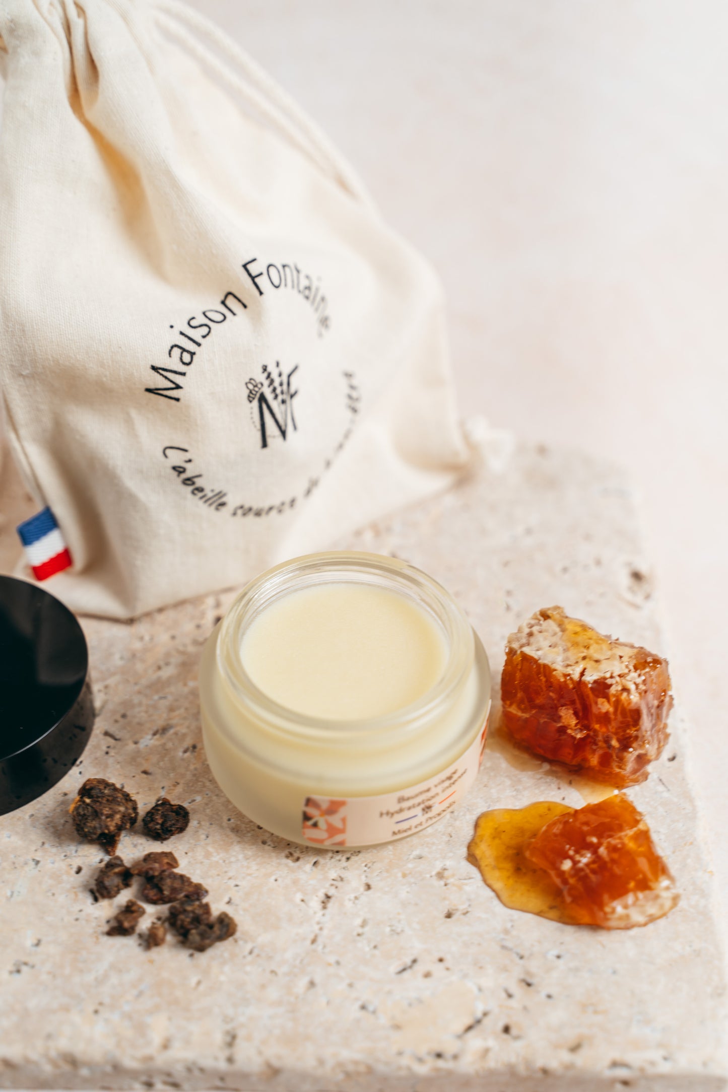 Le baume visage ouvert, posé sur une pierre avec son pochon, accompagné de propolis et de miel.
