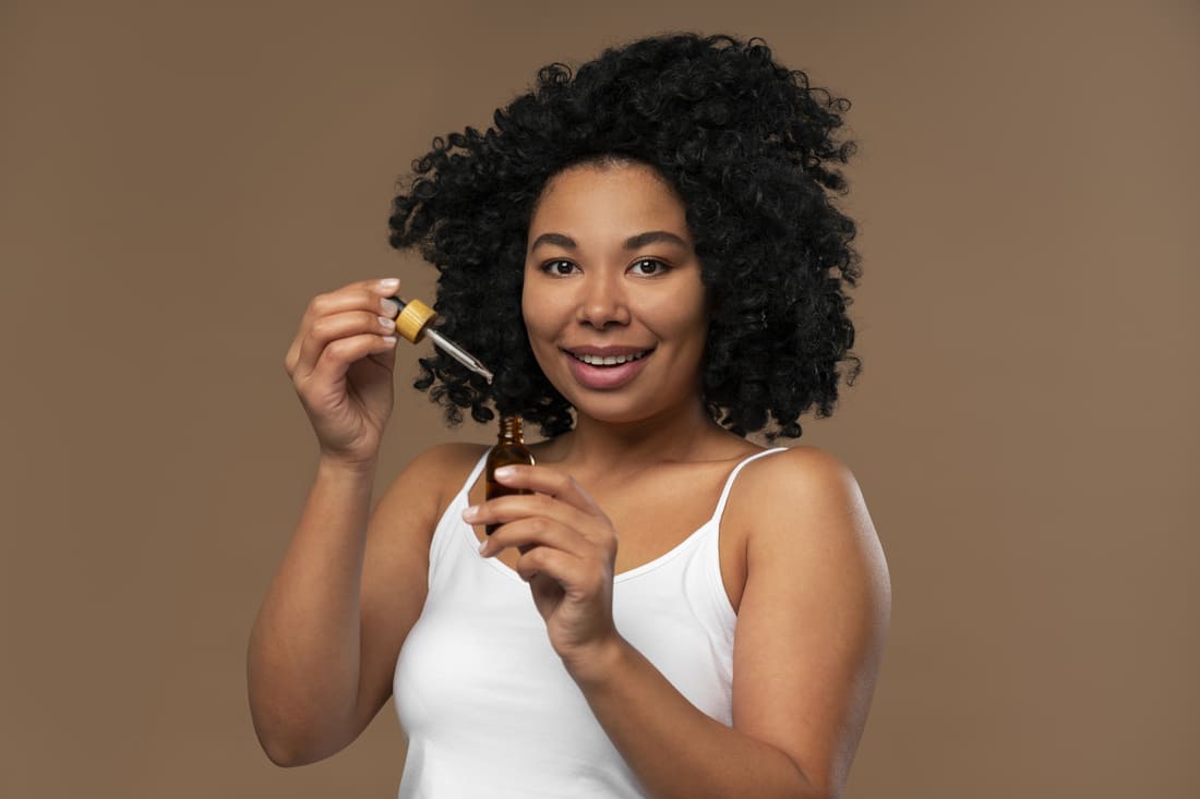 Une femme tenant de l'huile de macérât de propolis entre ses mains pour l'appliquer sur ses cheveux bouclés.