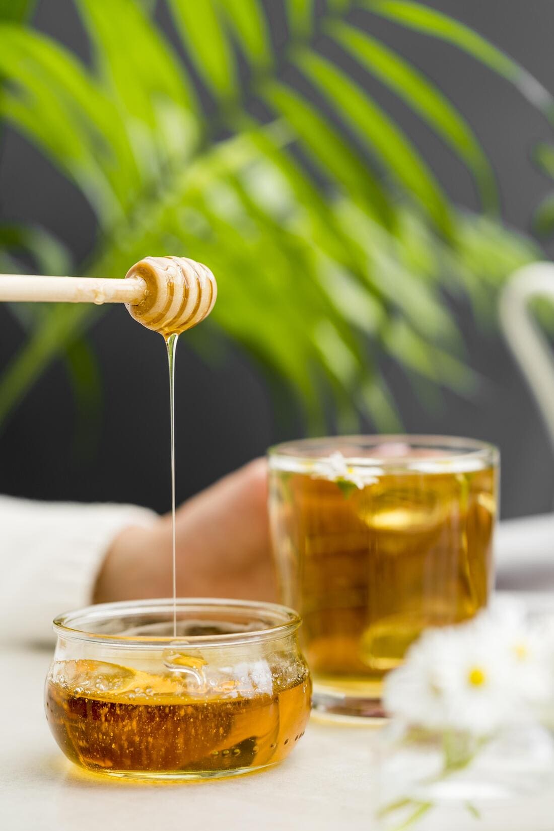 Image représentant une cuillère de miel d'où s'écoule un filet doré dans un pot en verre.